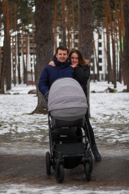 Genç bir aile kışın bebek arabasıyla parkta yürür. Mutlu aile fotoğrafı..