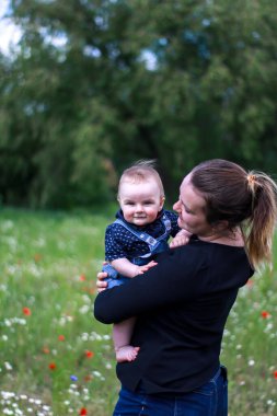 Koyu renk bluzlu bir anne ve tarlada kucağında küçük bir oğlan. Haşhaş tarlası. Doğa, bahar. Yaz günü.