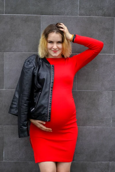 Young pregnant girl in a red dress in the parking lot. pregnancy is a joy. big pregnant belly. new life. — Stock Photo, Image