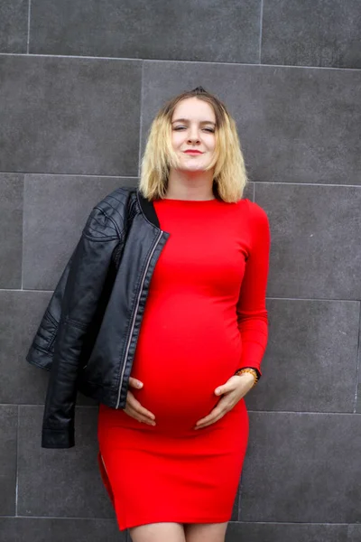 Jong zwanger meisje in een rode jurk op de parkeerplaats. zwangerschap is een vreugde. grote zwangere buik. nieuw leven. — Stockfoto