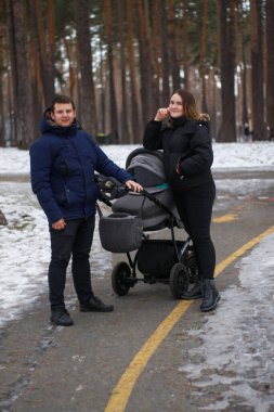 Genç bir aile kışın bebek arabasıyla parkta yürür. Mutlu aile fotoğrafı..