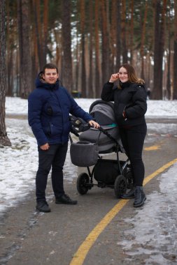 Genç bir aile kışın bebek arabasıyla parkta yürür. Mutlu aile fotoğrafı..