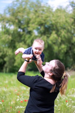 Koyu renk bluzlu bir anne ve tarlada kucağında küçük bir oğlan. Haşhaş tarlası. Doğa, bahar. Yaz günü.