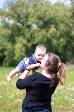 Koyu renk bluzlu bir anne ve tarlada kucağında küçük bir oğlan. Haşhaş tarlası. Doğa, bahar. Yaz günü.