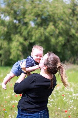 Koyu renk bluzlu bir anne ve tarlada kucağında küçük bir oğlan. Haşhaş tarlası. Doğa, bahar. Yaz günü.