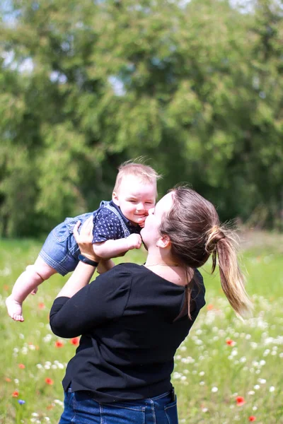 Koyu renk bluzlu bir anne ve tarlada kucağında küçük bir oğlan. Haşhaş tarlası. Doğa, bahar. Yaz günü.