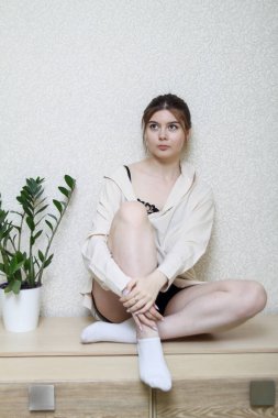 Evde oturan genç bir kız gömlekle oturuyor..