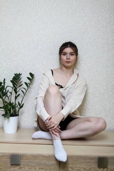 Uma jovem em um ambiente doméstico senta-se em uma camisa. — Fotografia de Stock