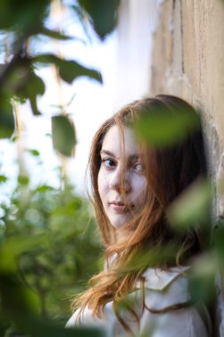 Ağaç yaprakları olan tuğla bir duvarın arka planındaki kız. Doğa ve yapının bir kombinasyonu. Canlı ya da cansız.