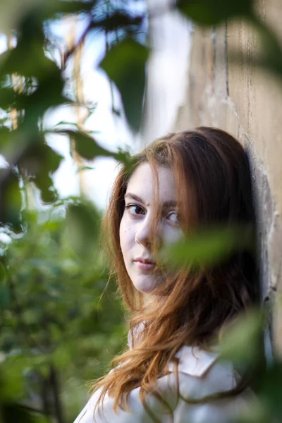 Fille sur un fond de mur de briques avec des feuilles d'arbre. une combinaison de nature et de construction. vivants et non vivants. — Photo