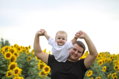 Esmer erkek baba ve tatlı çocuk sarışın oğul ayçiçeği tarlasında..