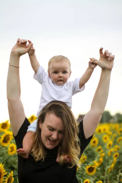 Brunette woman young mom with cute baby blonde son on a field of sunflowers. — Stock Photo, Image