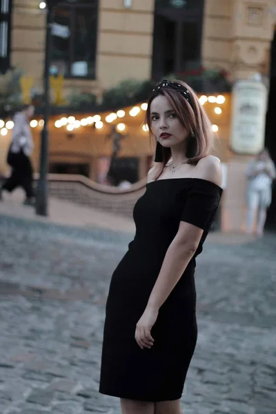 Mädchen in einem schwarzen kurzen Kleid auf der Abendstraße. vor dem Hintergrund von Lichtern, Geschäften. — Stockfoto