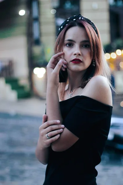 Menina em um vestido curto preto na rua da noite. contra o pano de fundo das luzes, lojas. — Fotografia de Stock