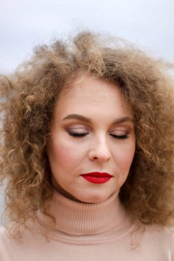 Çok üzgün, kıvırcık saçlı, yüzünde duygular olan parlak yağmurluklu bir kız..