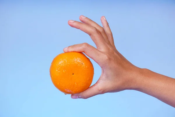 Foto Uma Mão Segurando Uma Laranja Com Fundo Azul — Fotografia de Stock