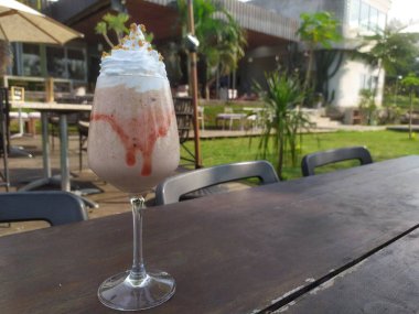 Açık havada uzun ve zarif bir şarap kadehinde sunulan krem şanti ve çikolata parçacıklarıyla kaplı kremalı çilekli milkshake. Yiyecek konsepti