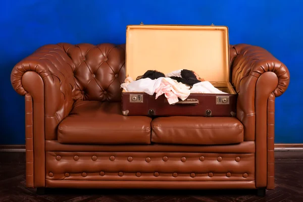 Старый чемодан с белье на древних кожаный диван — стоковое фото