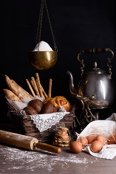 Assortimento di pane e pasticceria appena sfornati con uova, farina e teiera, su tavola rustica in legno . — Foto Stock