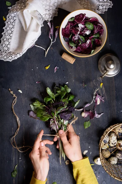 Eine Person bereitet einen gesunden Kräutersalat mit Basilikum, Radicchio und Wachteleiern zu. rustikaler Holztisch, Blick von oben. — Stockfoto