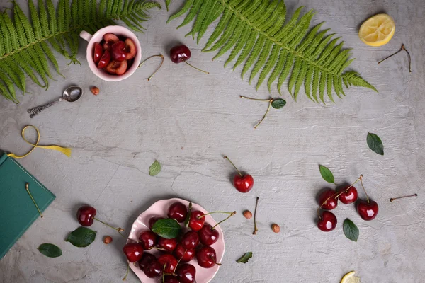 Vista aerea di ciliegie fresche su un piatto su superficie rustica. Frutta fresca su fondo grigio, decorata con felce e limone. Spazio di testo libero . — Foto Stock