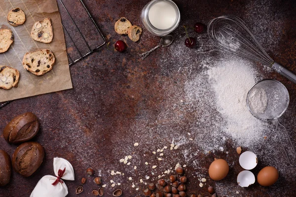 Bakery background, baking ingredients over rustic kitchen countertop. Baked cookies with hazelnuts, rye bread, milk and eggs. Top view, copy space.