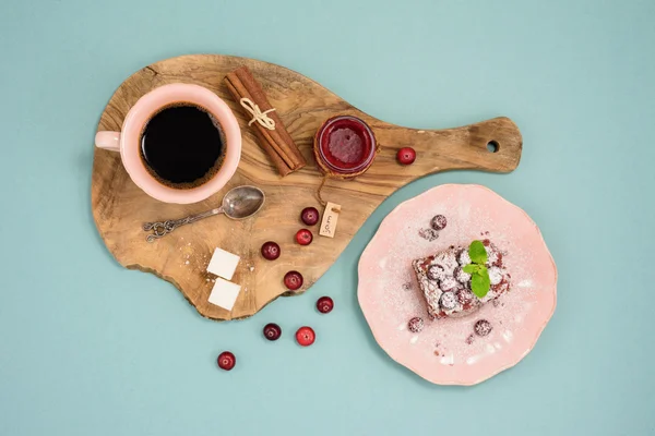 Kaffee und Schokoladenkuchen mit Preiselbeermarmelade und Zimt auf Holzbrett, vor türkisfarbenem Hintergrund. Ansicht von oben. — Stockfoto