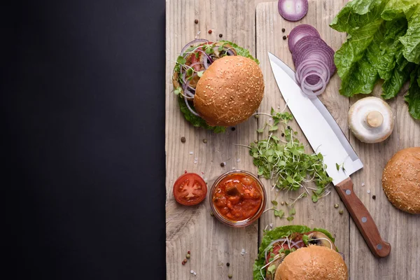 Hamburger freschi fatti in casa su una tavola di legno con ingredienti, vista dall'alto, spazio copia . — Foto Stock