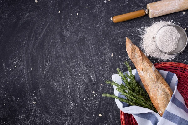 French Baguette con rosmarino avvolto in un asciugamano in cesto rosso e farina integrale, mattarello su fondo rustico. Vista dall'alto, spazio di copia, orizzontale . — Foto Stock