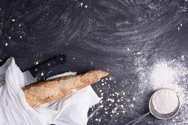 Pane fresco rustico avvolto in asciugamano bianco con farina e coltello su fondo scuro. Vista dall'alto, spazio per il testo . — Foto Stock