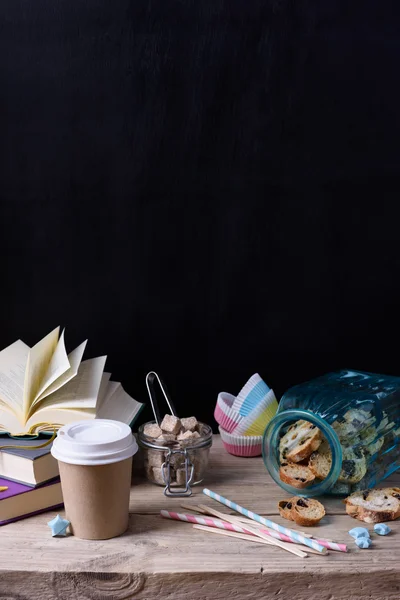 Stillleben-Kaffee zum Mitnehmen mit Keksen, Zucker und Büchern auf Holztisch und schwarzer Wand. Hipster-Stil. Kopierraum. — Stockfoto