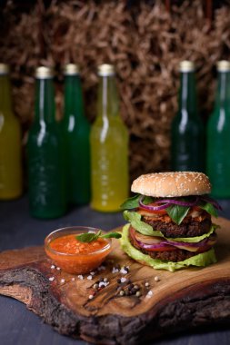 Homemade burger on wooden serving board with lemonade, spicy tomato sauce, sea salt and herbs.