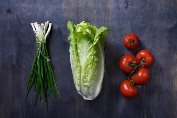 Receta de ensalada verde fresca ingredientes en la mesa de madera, pase por alto tiro. Lechuga, tomates, cebolla de primavera . — Foto de Stock