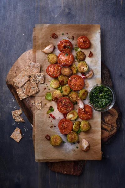 Grilled vegetables: tomatoes and brussels sprouts, garlic, chili pepper and crackers on rustic cutting board.