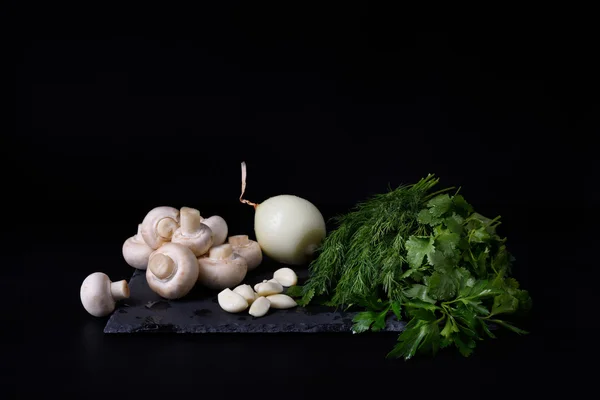 Verduras jóvenes de primavera en pizarra, fondo negro. Champiñones, eneldo, ajo, cebolla . — Foto de Stock