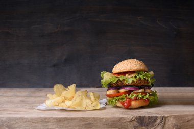 Sığır eti, domates, peynir, marul ve patates cipsi ahşap sayaçta lezzetli burger. Kopya alanı.