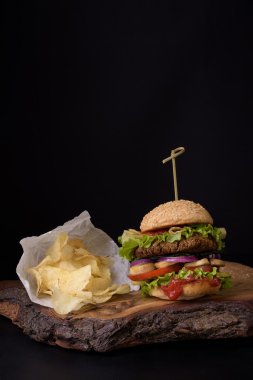 Kaba woden tahta, koyu arka plan üzerinde patates cipsi ile ev yapımı hamburger.