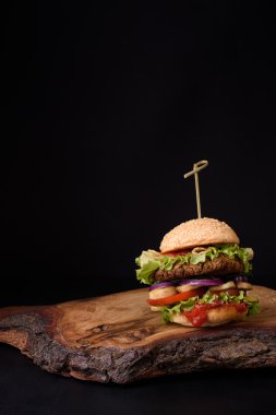 Rustik ahşap tahta, koyu arka plan üzerinde lezzetli ev yapımı hamburger. Kopya alanı.