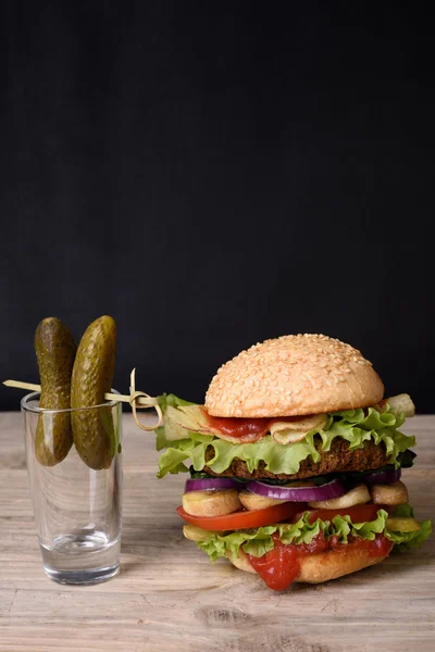 Delicious burger with pickles, beef, tomato, cheese and lettuce on wooden table, dark background.