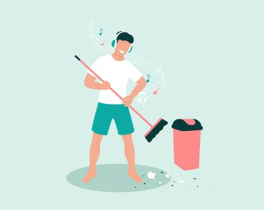 Genç erkek temizlikçi süpürge kullanıyor ve kulaklık konseptini kullanarak müzik dinlerken çöpü boşaltıyor.