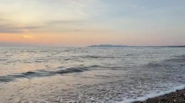 Adriyatik Denizi 'nin geniş gün batımı manzarası. Dalgalar çakıl taşı plajına doğru ilerliyor. Sıcak gökyüzü ve doğal okyanus hareketleriyle sakin bir akşam manzarası..