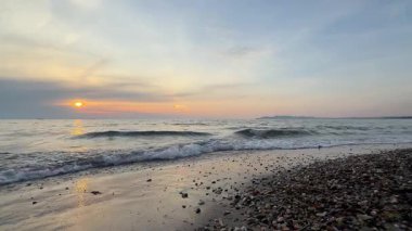 Adriyatik Denizi kıyısındaki çakıl taşlı bir plaja vuran yumuşak dalgaların üzerinde ılık gün batımı ışığı. Altın saatli atmosferi ve doğal deniz hareketleriyle huzurlu sahil manzarası.