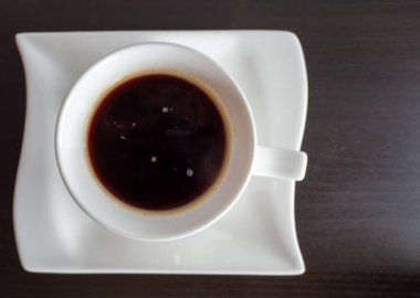 Tahta arka planda beyaz bir bardak sıcak içecek.