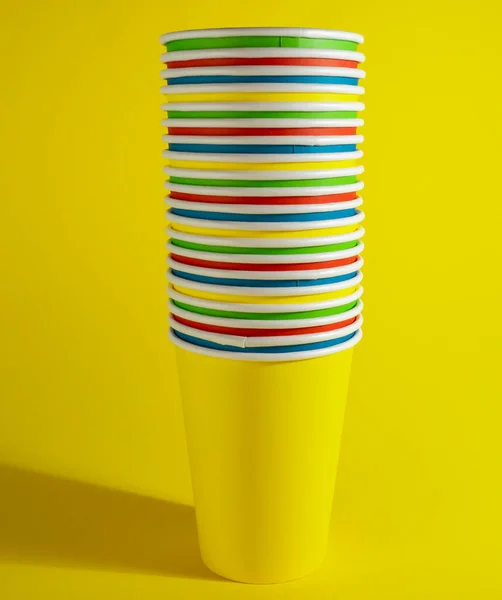 Multicolored paper cups, disposable cups on a yellow background.