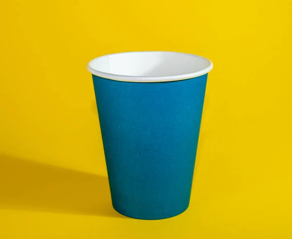 Šálek z modrého papíru, jednorázový šálek na žlutém pozadí. — Stock fotografie