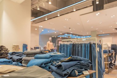 Almanya 7 Ekim 2025. Bir moda mağazasında sergilenen kot pantolon yığını. Arka planda günlük pantolon ve mankenlerle dolu askılar..