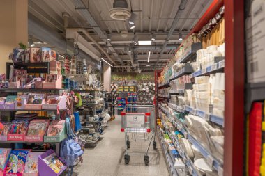 Almanya 2 Ekim 2025. Alışveriş arabalarıyla dolu bir süpermarket koridoru, renkli mutfak gereçleri ve kağıt eşyalarla dolu raflar. Parlak ışıklandırma geniş bir ürün yelpazesini vurgular.