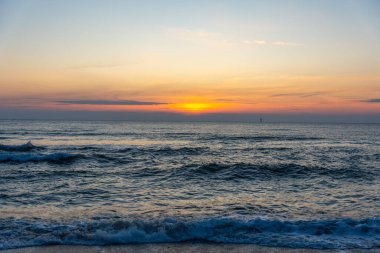 Dalgalar yavaşça içeri girerken güneş Kuzey Denizi 'nin üzerinde batıyor. Gökyüzünün renkleri suya yansıyor..
