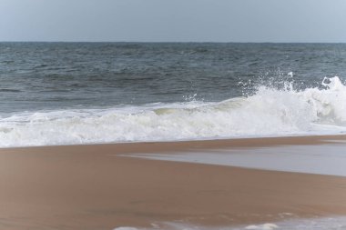 Sahilde dalga kırma. Kumlu sahilde beyaz bir dalga güçlü bir şekilde kırılır. Sprey ve su hareketi denizin dinamiklerini gösteriyor..