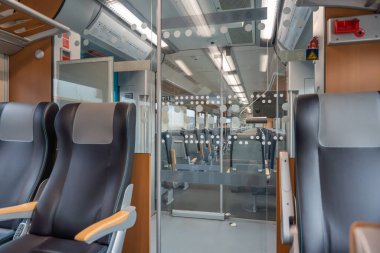 Cam kapı, tren manzarası. Deri tren koltukları bir sonraki vagona açılan cam sürgülü kapıya bakıyor. Parlak ışıklandırma, temiz ve modern tasarımı vurgular.